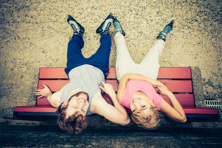 Young people friends in training suit with roller skates. Woman and man relaxing on bench outdoor.の写真素材