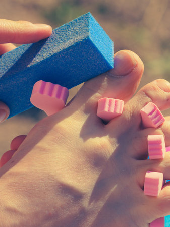 Unrecognizable woman doing pedicure during vacations outdoor on beach. Female buffing her foot nails...