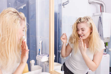 Happy woman in bathroom having wet long blonde hair. Playful young teenage female taking care of her hairdo.の写真素材