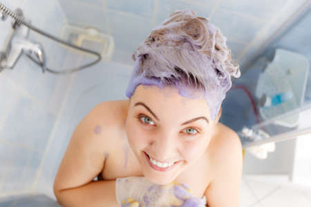 Woman applying coloring shampoo on her hair. Female having purple washing product. Toning blonde color at home.の写真素材