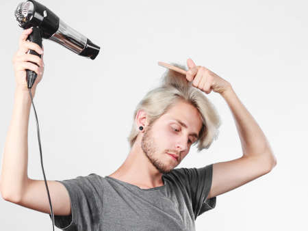 Hairstyle and fashion. Young trendy male hairstylist barber with new idea of look changing. Blonde man holding hair dryer and comb creating new hairdoの写真素材