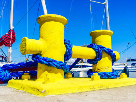 Shipping objects concept. Sailing ropes tied around yellow marina bollard. Outdoor shot on sunny day.の写真素材