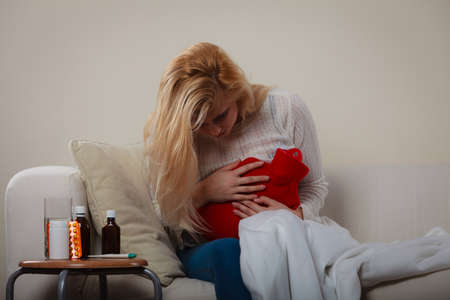 Painful periods and menstrual cramp problems concept. Woman feeling stomach cramps lying on cofa feeling very unwell.の写真素材