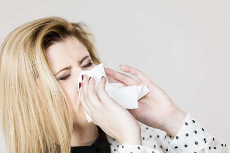 Sickness, seasonal virus problem concept. Woman being sick having flu sneezing into tissueの写真素材