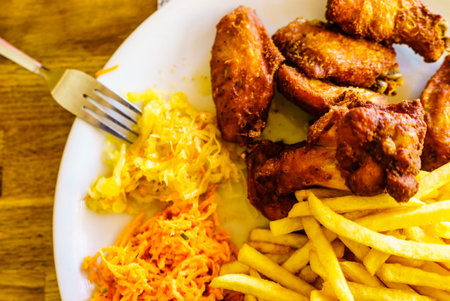 Close up of plate full of food. Chicken wings, french fries and salad. Delicious meal.の写真素材