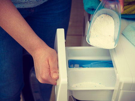 Washing powder detergent and measuring cup pouring into machine. Household duties, clothes laundry obejcts concept.の写真素材