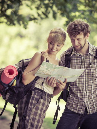 Man and woman tourists backpackers reading map on trip. Young couple hikers searching looking for...