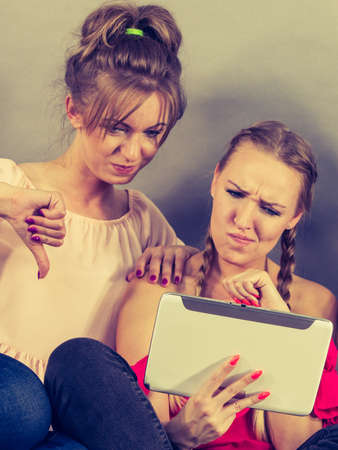 Women sitting on sofa having fun surfing on the internet using smart digital pc tablet modern device showing thumbs down.の写真素材