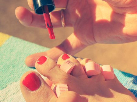 Woman relaxing doing her pedicure with red nail polish on beach towel. Female taking care of feet