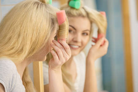 Blonde woman using hair rollers to create beautiful hairstyle on her hairdo.の写真素材