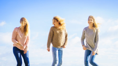 Three fashionable women wearing sweaters during warm autumnal weather spending their free time on...