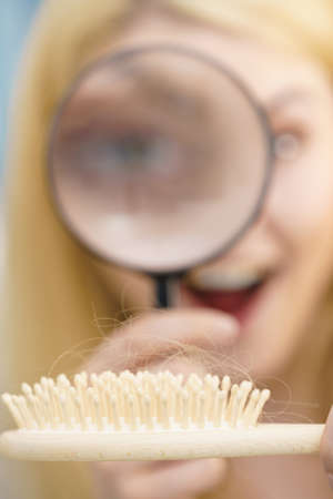Woman using magnifying glass looking at her brush. Examing hair loss, haircare concept.の写真素材