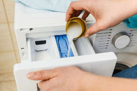 Liquid powder detergent and measuring cup pouring into machine. Household duties, clothes laundry obejcts concept.の写真素材