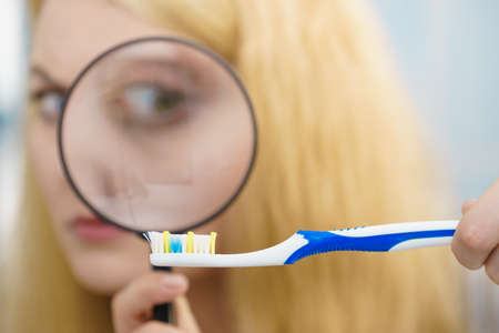 Beautiful perfectionist young woman checking her tooth brush through manifying loupe glass. Hygiene, bacteria, sterility concept.の写真素材