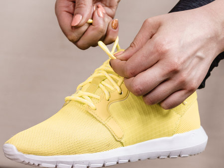 Woman in sportswear sitting on sofa indoor getting ready for exercises. Tying up shoes
