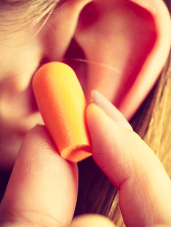 Woman putting ear plugs into her ears getting rid on noise in loud place.の写真素材