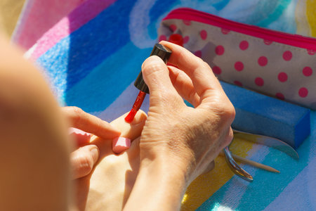 Woman relaxing doing her pedicure with red nail polish on beach towel. Female taking care of feet