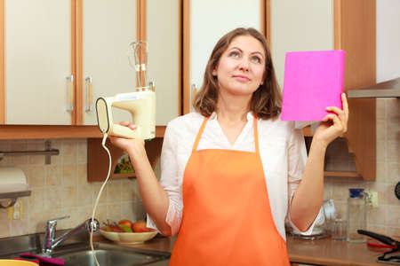 Housewife thinking and planning meal food. Mature woman chef cook with cookbook and mixer.の写真素材