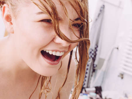 Happy woman in bathroom having wet long blonde hair. Playful young teenage female taking care of her hairdo.の写真素材