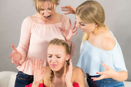 Woman being bullied by her two female friends. Women having argument. Angry fury girls screaming at her friend or younger sister. Friendship difficulties, rivaly and envy problems.の写真素材