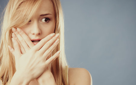 Closeup young amazed woman wide eyed covering her mouth with hands on  blue