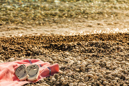 Beach accessories on a towel for sunbathing. Shoes sandals flip flops, stone rocks sand.の写真素材