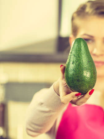 Woman holding green vegetable, delicious avocado. Female wearing apron in kitchen making food.の写真素材