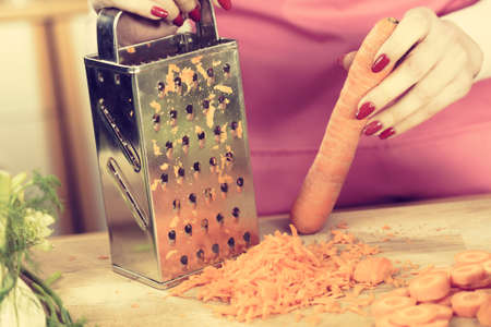 Unrecognizable woman grating carrot on metal grater, kitchen utensil making food preparing healthy vegetable salad.の写真素材