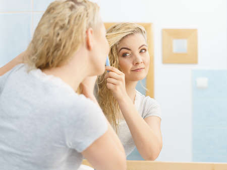 Pretty young woman taking care of haircare, brushing wet blonde hair after taking a shower feeling fresh.の写真素材