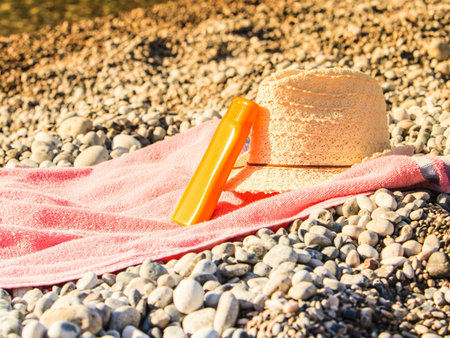 Beach accessories on a towel for sunbathing. Sunny hat and sunscreen orange bottle, stone rocks...