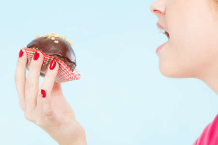 Diet, sweets, food concept. Woman holding delicious chocolate cupcake with peanut frosting about to take biteの写真素材