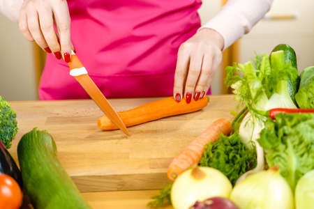 Woman cutting, preparing vegetable, delicious sweet carrot using kitchen knife. Female hands making food.の写真素材