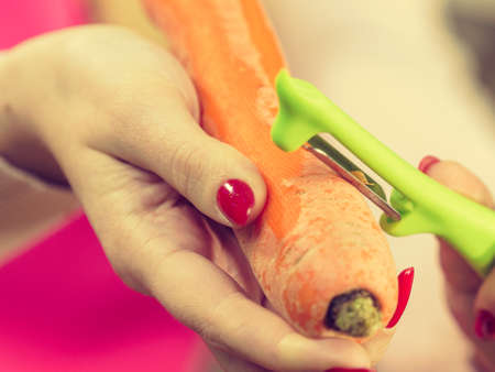 Woman peeling vegetables using food peeler. Cooking female preparing carrot before serving.の写真素材