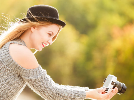 Smiling woman wearing black hat and grey sweater taking pictures using digital camera on outdoor...