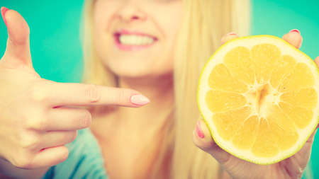Woman smiling girl holding half of yellow grapefruit citrus fruit in hand, pointing with finger, recommending healthy eating, on green. Dieting losing weight concept.の写真素材