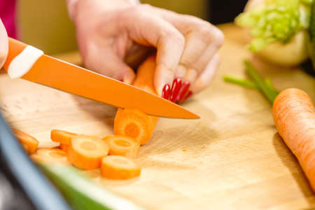 Woman cutting, preparing vegetable, delicious sweet carrot using kitchen knife. Female hands making food.の写真素材