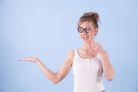Elegant young woman pretending wearing funny nerd eyeglasses showing copy space on hand. Education and studying females look concept.の写真素材
