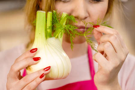 Woman in kitchen holding green fresh raw fennel bulb vegetable. Housewife cooking meal. Healthy eating, vegetarian food, dieting concept.の写真素材