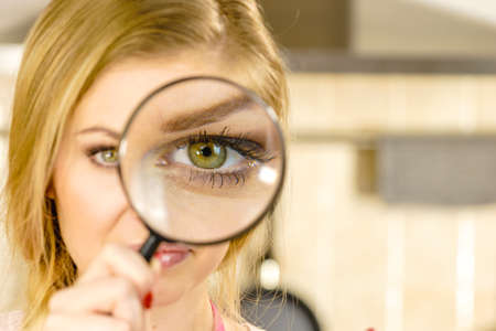 Blonde woman holding magnifying glass investigating something and looking closely, trying to find solution.の写真素材
