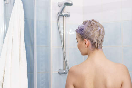 Woman having purple shampoo foam on her head under the shower. Female toning blonde hair using colored shampoo.の写真素材