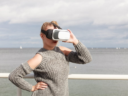 Young woman testing VR glasses outside. Female wearing virtual reality headset during spring...