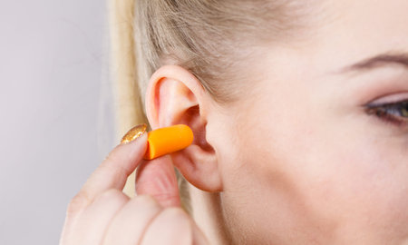 Woman putting ear plugs into her ears getting rid on noise in loud place.