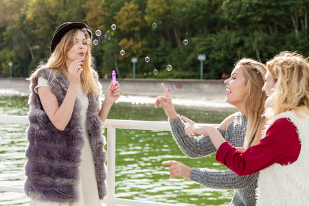 Vacations joy, friendship concept. Women friends having fun blowing soap bubbles outdoor.