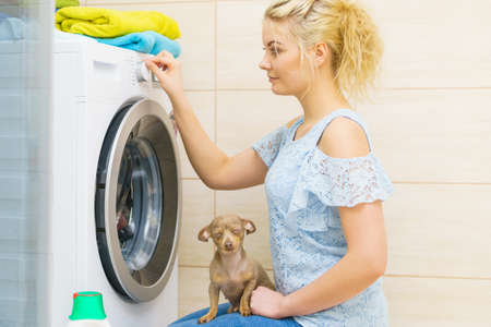 Young blonde woman setting washing clothes laundry machine knob, choosing program. Household duties concept.の写真素材