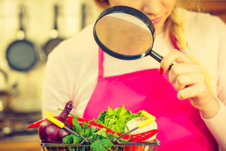Woman using magnifying glass loupe, investigating shopping basket with many colorful vegetables. Healthy eating lifestyle, nutrients vegetarian food, searching for pesticides and chemicals.の写真素材