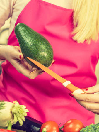 Woman cutting, preparing green vegetable, delicious avocado using kitchen knife. Female wearing apron making food.の写真素材