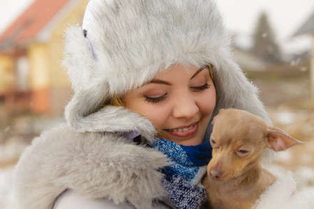 Young woman having fun outside in snow. Female playing with her small purebreed dog puppy in cold winter day.の写真素材