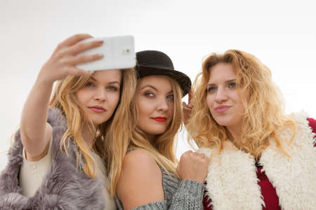 Three females taking selfies, having fun outdoor using smart phone to take photo.の写真素材