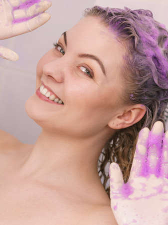 Woman applying coloring shampoo on her hair. Female having purple washing product. Toning blonde color at home.の写真素材