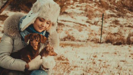 Young woman having fun outside in snow. Female playing with her small purebreed dogs puppies in cold winter day.の写真素材